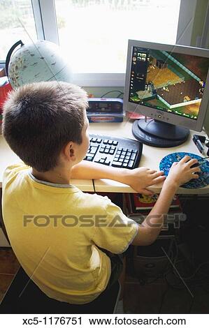 Stock Image - 9 years old boy playing at pc. Fotosearch