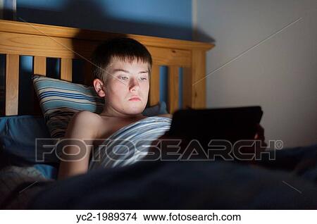 A 13 year old teenage boy using a tablet on the internet in bed. View Large Photo Image Picture - A 13 year old teenage boy using a tablet on the internet in bed.. Fotosearch