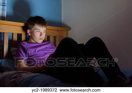Stock Image - A 13 year old teenage boy using a tablet on the internet in bed.. Fotosearch
