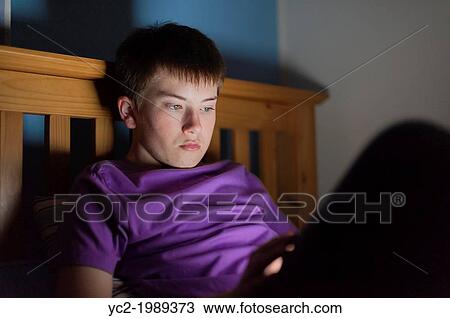 Stock Image - A 13 year old teenage boy using a tablet on the internet in bed.. Fotosearch