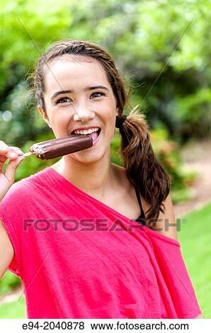 A 14 year old brunette girl eating a chocolate ice cream bar in a park setting. View Large Photo Image Stock Photo - A 14 year old brunette girl eating a chocolate ice cream bar in a park setting.. Fotosearch