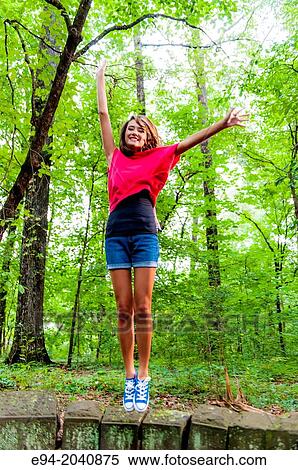 A 14 year old brunette girl in shorts, sneakers and a red top in a forest setting jumping of a rock wall. View Large Photo Image Stock Photography - A 14 year old brunette girl in shorts, sneakers and a red top in a forest setting jumping of a rock wall.. Fotosearch