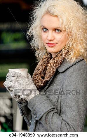 Stock Photo - A 22 year old blond woman sitting at an outdoor cafe with a cup of coffee in the winter.. Fotosearch