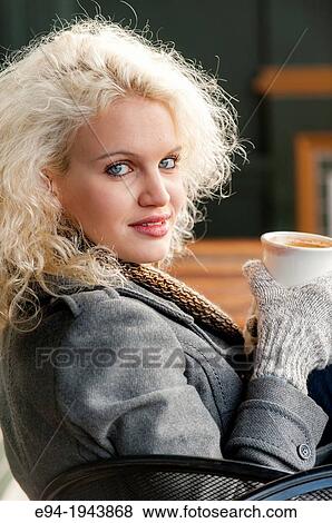 Stock Photo - A 22 year old blond woman sitting at an outdoor cafe with a cup of coffee in the winter.. Fotosearch