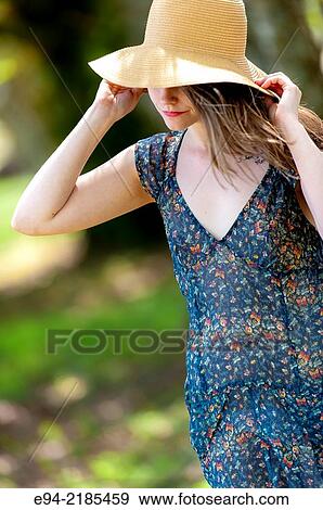 Stock Photo - A 22 year old brunette woman walking by old trees in a pasture wearing a straw hat and dress looking down.. Fotosearch