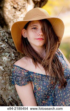 A 22 year old brunette woman wearing a summer dress and a straw hat looking directly at the camera, outdoors. View Large Photo Image Picture - A 22 year old brunette woman wearing a summer dress and a straw hat looking directly at the camera, outdoors.. Fotosearch