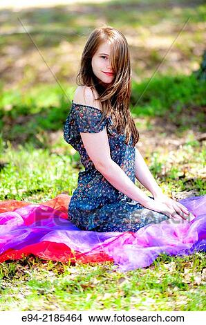 A 22 year old brunette woman wearing a summer dress sitting on a blanket in a pasture. View Large Photo Image Picture - A 22 year old brunette woman wearing a summer dress sitting on a blanket in a pasture.. Fotosearch