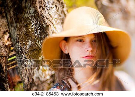 Stock Image - A 22 year old brunette woman wearing a summer dress and a straw hat looking directly at the camera, outdoors.. Fotosearch