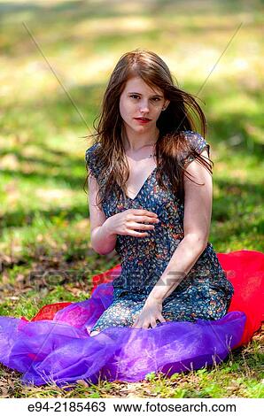 Stock Image - A 22 year old brunette woman wearing a summer dress sitting on a blanket in a pasture.. Fotosearch