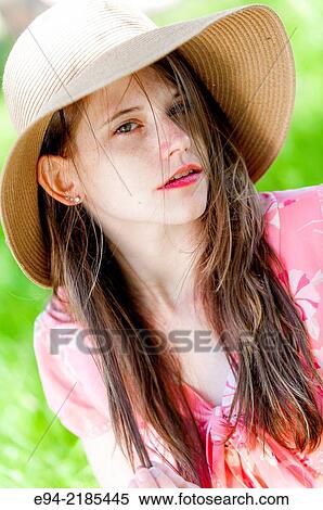 Stock Photography - A 22 year old brunette woman wearing a straw hat looking directly at the camera, outdoors.. Fotosearch