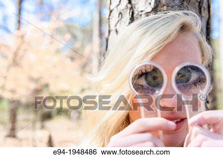A 23 year old blond woman holding magnifying glasses in front of her face causing distortion of her eyes. View Large Photo Image Stock Photograph - A 23 year old blond woman holding magnifying glasses in front of her face causing distortion of her eyes.. Fotosearch