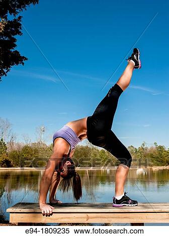 A 23 year old brunette woman in workout clothing doing a back bend on a bench by a pond View Large Photo Image Stock Photography - A 23 year old brunette woman in workout clothing doing a back bend on a bench by a pond. Fotosearch