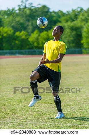 Stock Image - A 24 year old black man wearing soccer clothing bouncing a soccer ball off his knee.. Fotosearch
