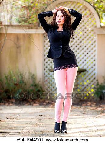 Stock Image - A 24 year old woman brunette woman in a black top, pink leggings and high heels outdoors.. Fotosearch