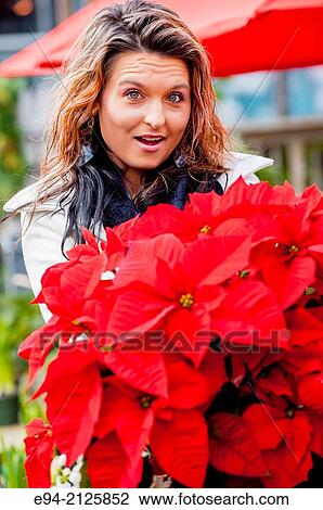 Stock Image - A 27 year old brunette woman shopping for holiday poinsettia plants at an outdoor shop.. Fotosearch
