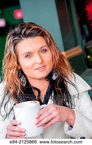 A 27 year old brunette woman sitting at an outdoor cafe and holding a white mug of hot chocolate looking at the camera. View Large Photo Image Stock Photograph - A 27 year old brunette woman sitting at an outdoor cafe and holding a white mug of hot chocolate looking at the camera.. Fotosearch