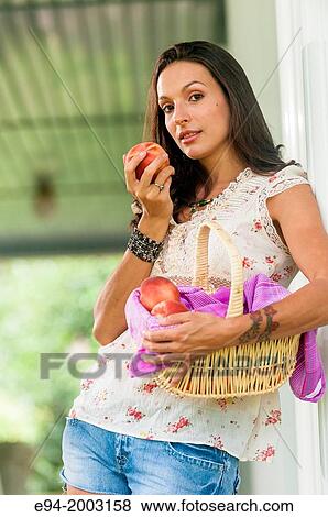 A 27 year old brunette woman wearing cut off shorts standing on a porch holding a basket of peaches. View Large Photo Image Stock Photo - A 27 year old brunette woman wearing cut off shorts standing on a porch holding a basket of peaches.. Fotosearch