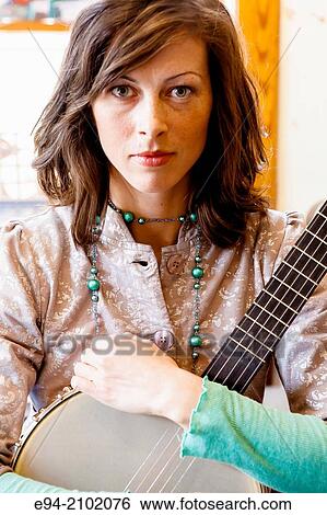 Stock Photograph - A 28 year old brunette woman holding a banjo on her lap with a serious expression.. Fotosearch