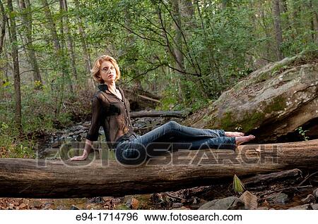 A 29 year old blond woman in a forest sitting a on log wearing blue jeans and a black see-through top View Large Photo Image Stock Photograph - A 29 year old blond woman in a forest sitting a on log wearing blue jeans and a black see-through top. Fotosearch