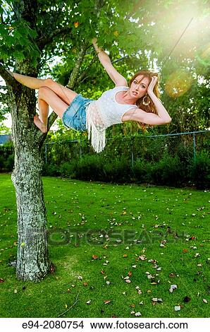A 31 old redhead woman hanging from tree branches in a backyard. View Large Photo Image Picture - A 31 old redhead woman hanging from tree branches in a backyard.. Fotosearch
