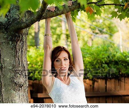 Stock Image - A 31 old redhead woman hanging from tree branches in a backyard.. Fotosearch