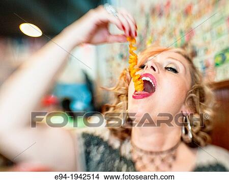 A 34 year old blond woman with mouth open and head back putting a curly french fry in her mouth. View Large Photo Image Picture - A 34 year old blond woman with mouth open and head back putting a curly french fry in her mouth.. Fotosearch