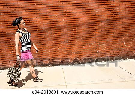 A 35 year old brunette woman walking on sidewalk in front of a brick wall. View Large Photo Image Stock Image - A 35 year old brunette woman walking on sidewalk in front of a brick wall.. Fotosearch