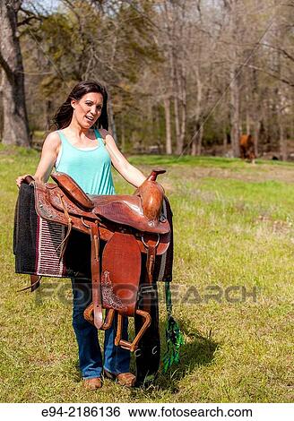 A 36 year old brunette woman carrying a saddle in a pasture. View Large Photo Image Stock Photograph - A 36 year old brunette woman carrying a saddle in a pasture.. Fotosearch