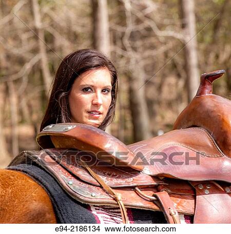 A 36 year old brunette woman looking over the saddle on a horse. View Large Photo Image Picture - A 36 year old brunette woman looking over the saddle on a horse.. Fotosearch