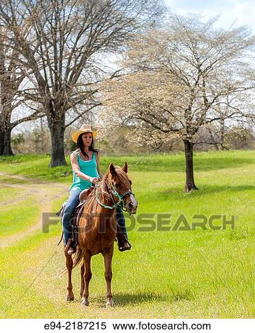 A 36 year old brunette woman wearing jeans and a straw hat riding a horse on a farm. View Large Photo Image Stock Photography - A 36 year old brunette woman wearing jeans and a straw hat riding a horse on a farm.. Fotosearch