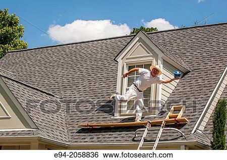 Stock Photograph - A 45 year old man on a roof balancing on one leg clowning around while painting a house.. Fotosearch