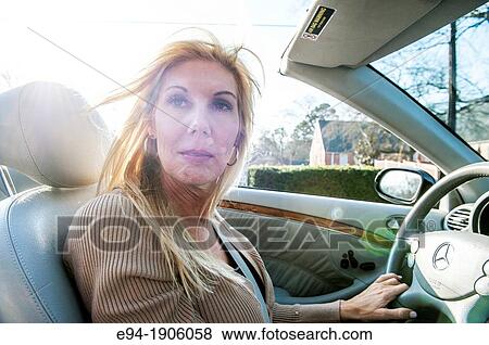 Stock Photo - A 48 year old blond woman talking and being expressive while driving her convertible car. Fotosearch