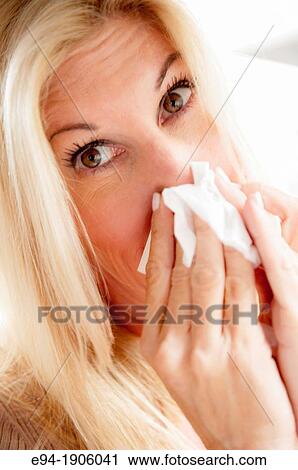 Stock Image - A 48 year old blond woman wiping her nose with a tissue, looking at the camera. Fotosearch