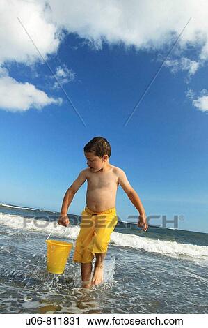 Stock Image - a 5 yr old boy carrying a pail of water at the beach. Fotosearch