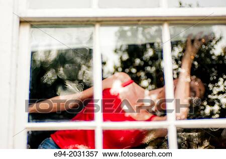 Stock Photo - A 51 year old brunette woman looking out of a window, face partially obscured.. Fotosearch