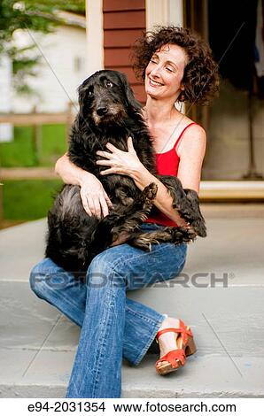 A 51 year old brunette woman wearing jeans sitting on steps in front of her house playing with her dog. View Large Photo Image Picture - A 51 year old brunette woman wearing jeans sitting on steps in front of her house playing with her dog.. Fotosearch