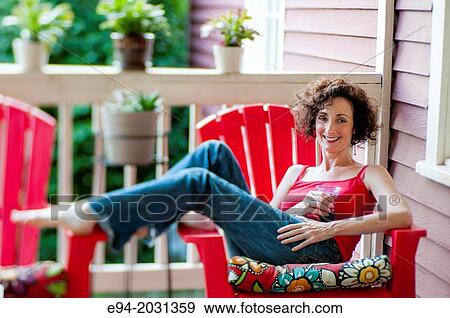 A 51 year old brunette woman wearing jeans and a red top lounging on her back porch with a drink. View Large Photo Image Stock Photo - A 51 year old brunette woman wearing jeans and a red top lounging on her back porch with a drink.. Fotosearch