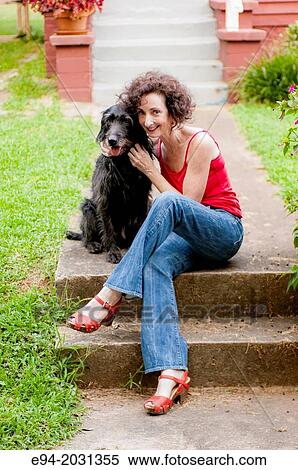 A 51 year old brunette woman wearing jeans sitting on steps in front of her house playing with her dog. View Large Photo Image Stock Photography - A 51 year old brunette woman wearing jeans sitting on steps in front of her house playing with her dog.. Fotosearch