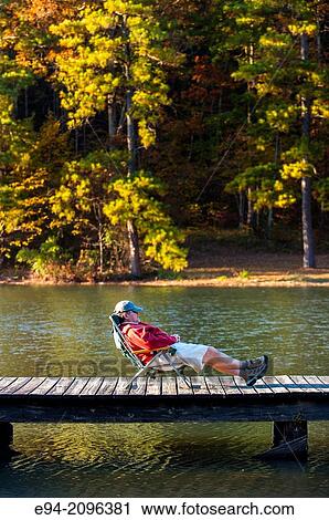 A 53 year old man lounging on a folding chair on a wooden dock by a lake with fall foliage in the background. Oak Mountain State Park, Alabama. View Large Photo Image Stock Image - A 53 year old man lounging on a folding chair on a wooden dock by a lake with fall foliage in the background. Oak Mountain State Park, Alabama.. Fotosearch