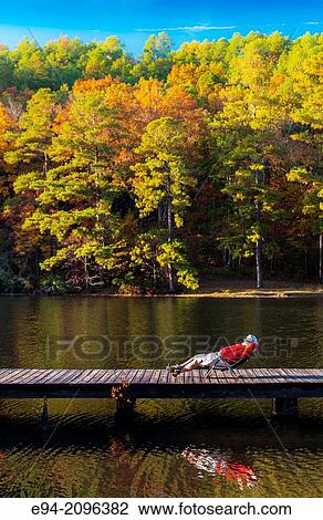 A 53 year old man lounging on a folding chair on a wooden dock by a lake with fall foliage in the background. Oak Mountain State Park, Alabama. View Large Photo Image Stock Image - A 53 year old man lounging on a folding chair on a wooden dock by a lake with fall foliage in the background. Oak Mountain State Park, Alabama.. Fotosearch