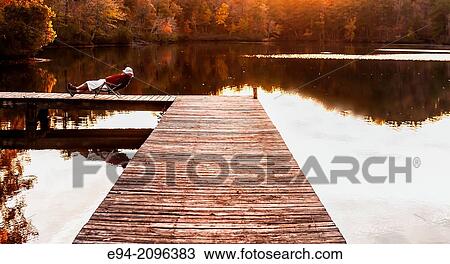 A 53 year old man lounging on a folding chair on a wooden dock by a lake with fall foliage in the background. Oak Mountain State Park, Alabama. View Large Photo Image Stock Image - A 53 year old man lounging on a folding chair on a wooden dock by a lake with fall foliage in the background. Oak Mountain State Park, Alabama.. Fotosearch
