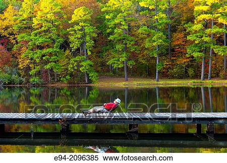 A 53 year old man lounging on a folding chair on a wooden dock by a lake with fall foliage in the background. Oak Mountain State Park, Alabama. View Large Photo Image Stock Photography - A 53 year old man lounging on a folding chair on a wooden dock by a lake with fall foliage in the background. Oak Mountain State Park, Alabama.. Fotosearch