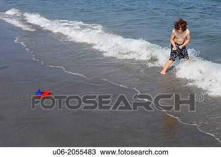 A 7 year old boy playing with a toy boat on a string in the waves at a beach at the sea View Large Photo Image Stock Image - A 7 year old boy playing with a toy boat on a string in the waves at a beach at the sea. Fotosearch