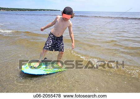 A 7 year old boy standing on a surf board in the waves at a beach at the sea View Large Photo Image Stock Photo - A 7 year old boy standing on a surf board in the waves at a beach at the sea. Fotosearch