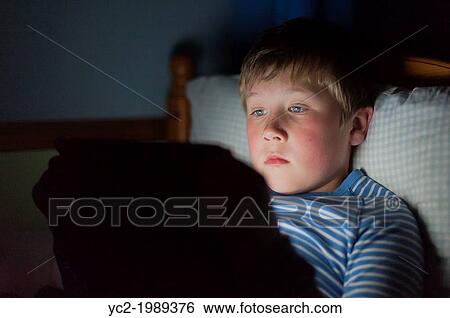 Stock Photograph - A 9 year old boy using a tablet on the internet in bed.. Fotosearch