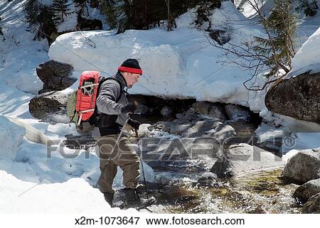 A adult male hiker crosses a river on a hiking trail in the White Mountains, New Hampshire USA during the spring months View Large Photo Image Stock Photo - A adult male hiker crosses a river on a hiking trail in the White Mountains, New Hampshire USA during the spring months. Fotosearch