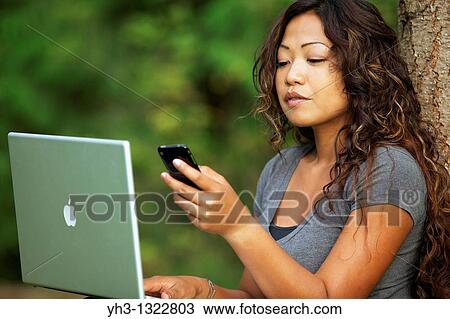 A beautiful African American woman using a Macbook Pro laptop while holding an iphone View Large Photo Image Stock Image - A beautiful African American woman using a Macbook Pro laptop while holding an iphone. Fotosearch