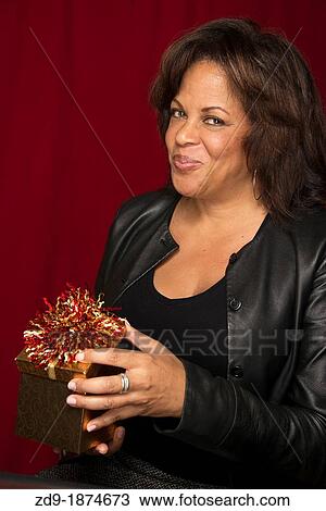 A beautiful middle-aged black woman opens a gift box with a wry grin View Large Photo Image Stock Image - A beautiful middle-aged black woman opens a gift box with a wry grin. Fotosearch