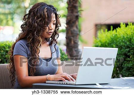 Stock Photography - A beautiful woman using laptop while holding a smartphone. Fotosearch