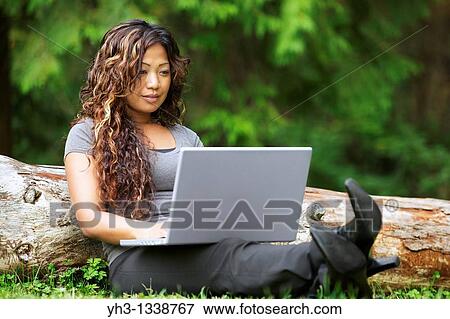 A beautiful young African American woman working on her laptop while sitting on a grass View Large Photo Image Stock Photo - A beautiful young African American woman working on her laptop while sitting on a grass. Fotosearch